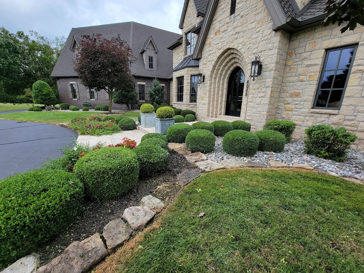 Stone home with neatly kept boxwood beds and a fresh lawn by Turf Works